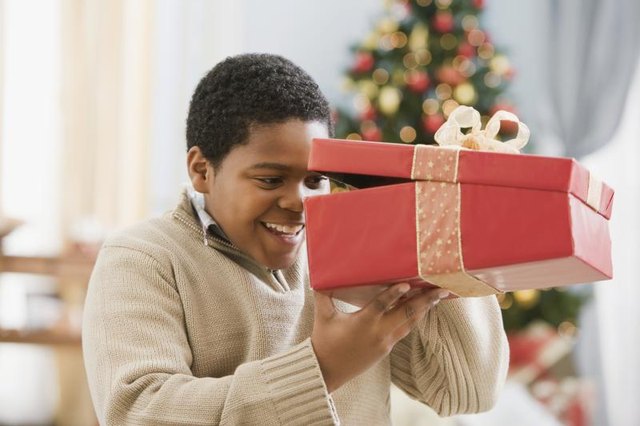 Young boy peeking into a box in front of a Christmas tree. Young boy peeking into a box in front of a Christmas tree.