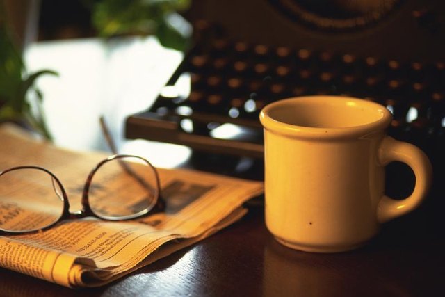 Typewriter, glasses, newspaper, and coffee mug on table. Typewriter, glasses, newspaper, and coffee mug on table.
