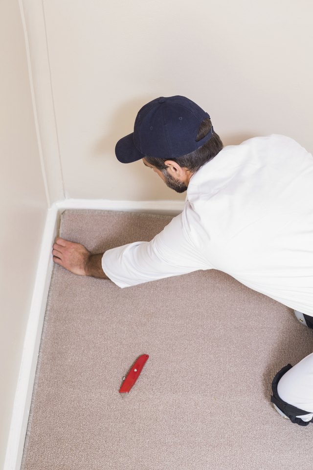 A man installs carpeting near a wall corner.