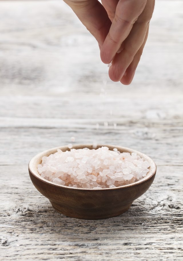 A woman takes a pinch of salt from a small bowl.