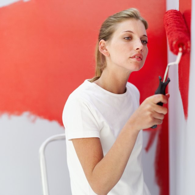 Close-up of woman painting a wall red.