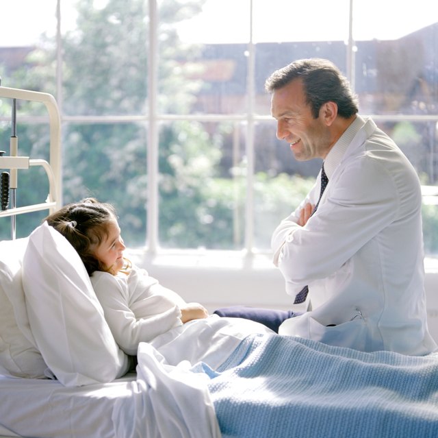 Doctor talking to female child in hospital bed.