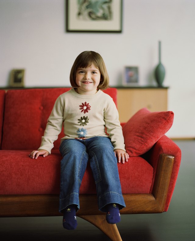 A girl sits on a red couch in a contemporary home.