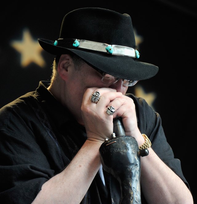 John Popper plays the harmonica while holding the microphone.