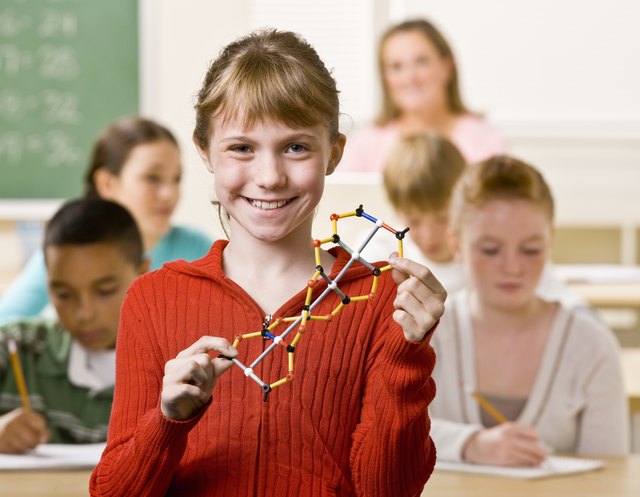 A smiling student holding a double helix model in a crowded classroom.