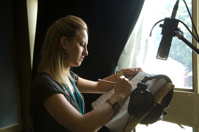 A woman writes song lyrics in a studio.