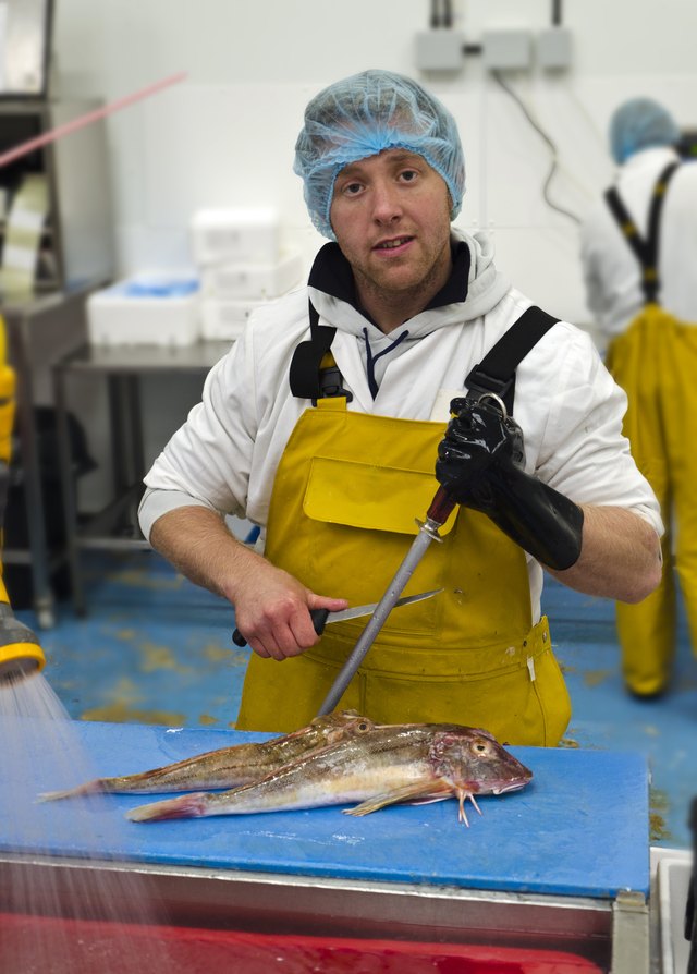 A worker in a fish market wears a hair net, gloves, and apron.
