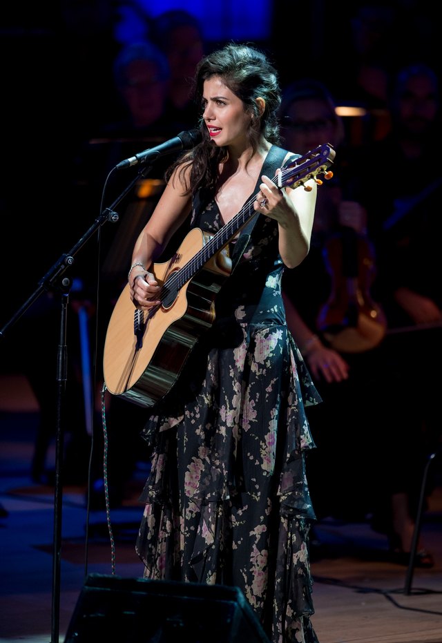 A performer sings and plays the acoustic guitar on a stage. A performer sings and plays the acoustic guitar on a stage.