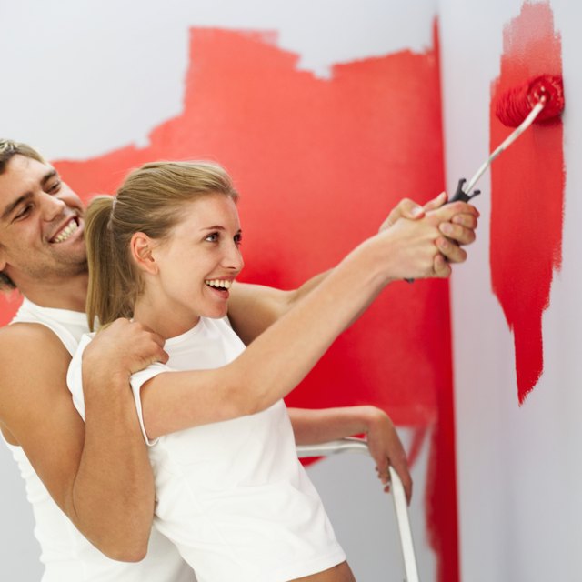 Young couple painting bedroom wall together.