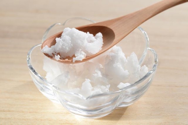 A small bowl of coconut oil being scooped with a wooden spoon. A small bowl of coconut oil being scooped with a wooden spoon.