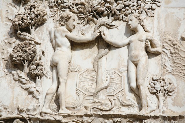 A close-up of a relief sculpture of Adam and Eve holding the serpent in the garden.