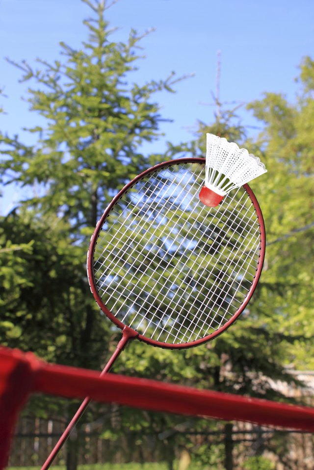 A badminton racket makes contact with a shuttle close to the net.