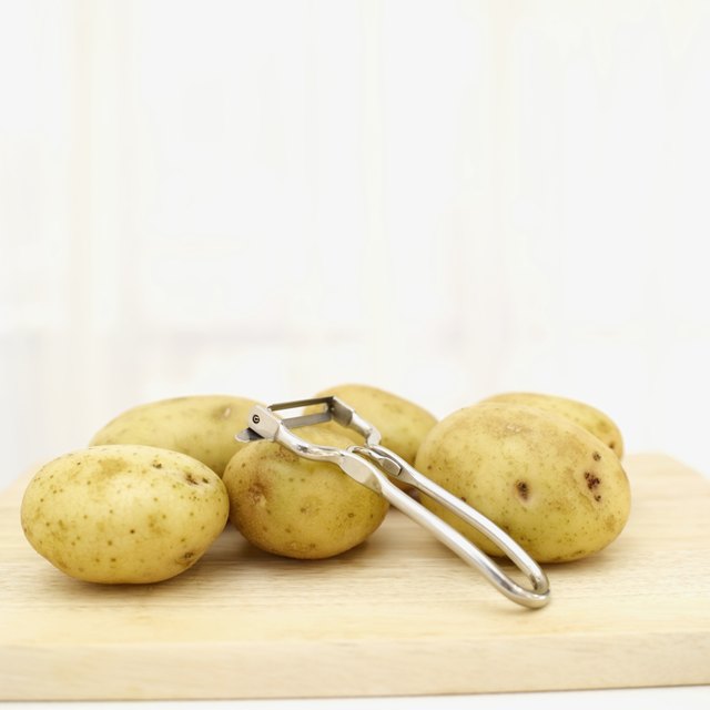 Small potatoes and peeler on cutting board.