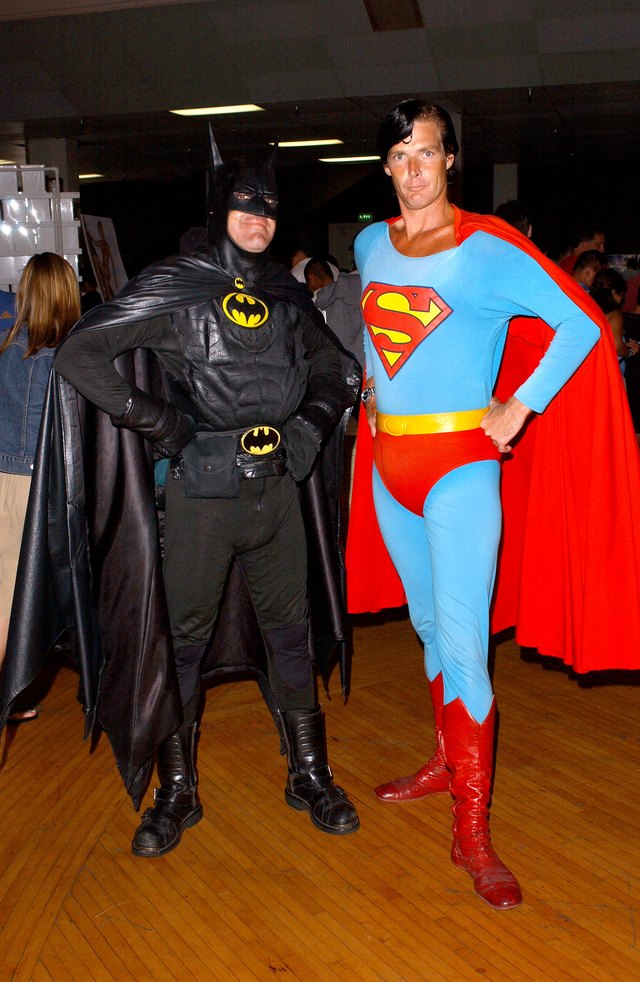 Two men dressed as Batman and Superman pose for a photo at a tradeshow.