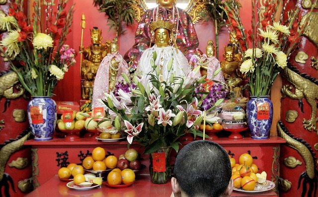 A man prays in front of the statues on a typical temple shrine.