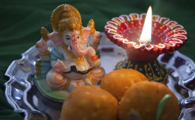 A Ganesh statue, prayer candle, and sweet treats on a plate.