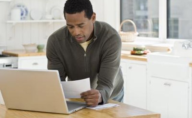 Man using laptop, reading paperwork