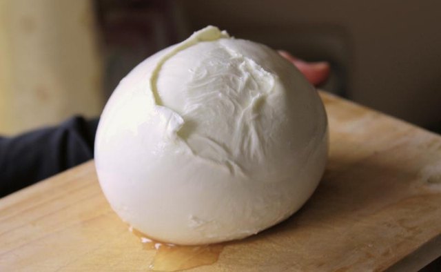 A ball of mozzarella cheese on a wood cutting board.