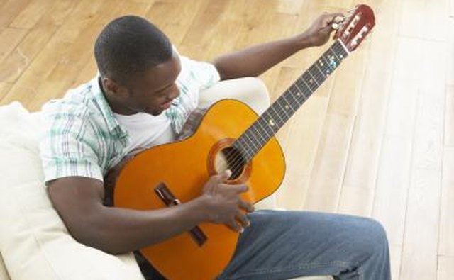 Guitar player tuning guitar on couch.