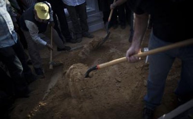 People shovel dirt at funeral