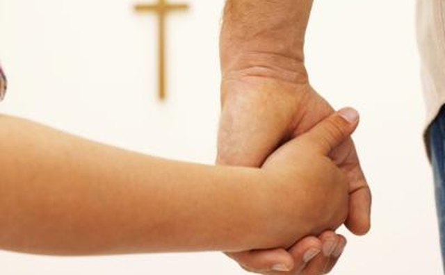 Parent and child holding hands, cross in background.