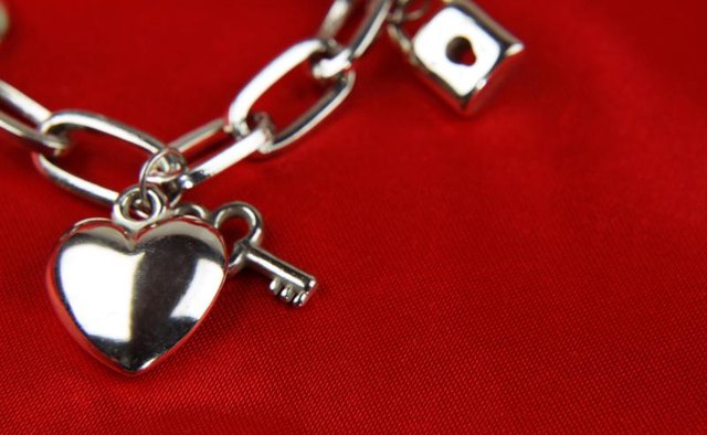 Charms on a charm bracelet, laying on red fabric.