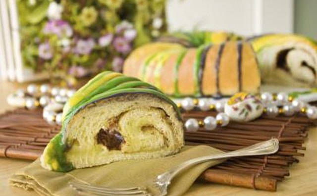 A slice of New Orleans king cake on a wooden mat with decorative beads.