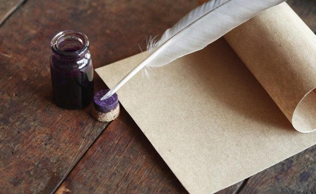 Ink, quill pen and scroll on a wooden table.