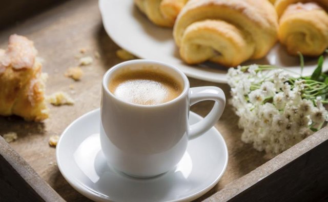 A cup of coffee on a tray next to a plate of croissants