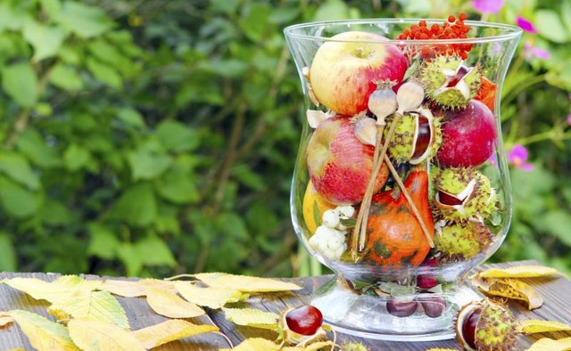 A glass vase filled with seasonal fruit and flowers.