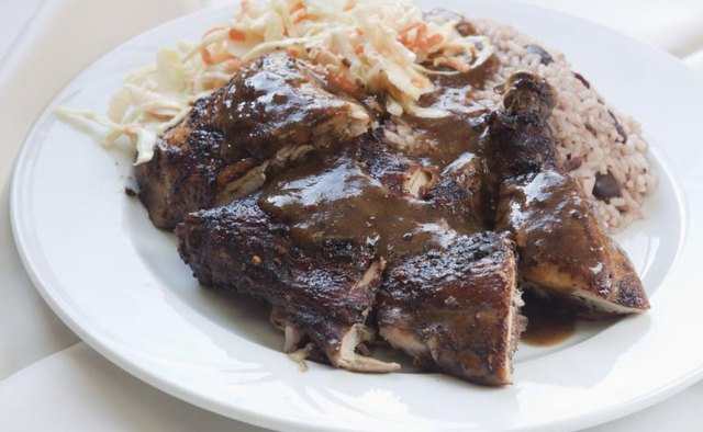 A plate of jerk chicken with rice, beans and coleslaw.