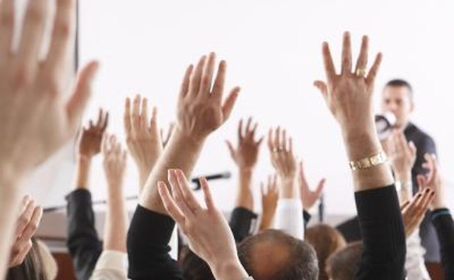 People raising hands in meeting.