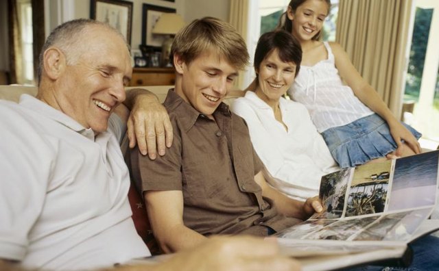 A man looking at a photo album with his family on the sofa.