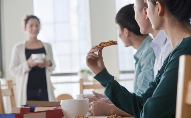 A woman joining a group eating pizza at a table.