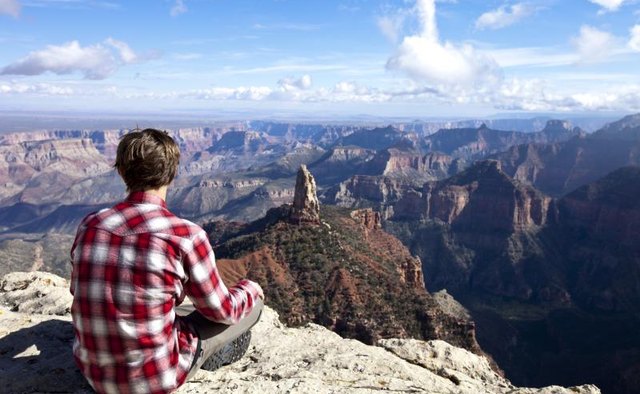 A young man sitting on a rock to take in the view.