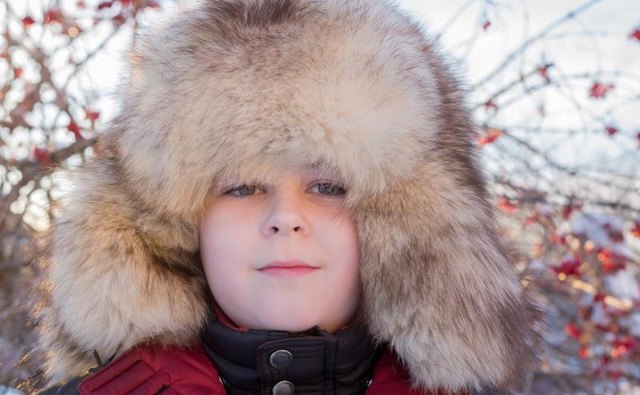 A portrait of a boy in a thick fur hat.