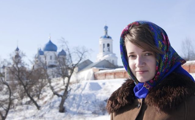 A woman wearing a fur-lined coat and a babushka tied around her face in the snow.