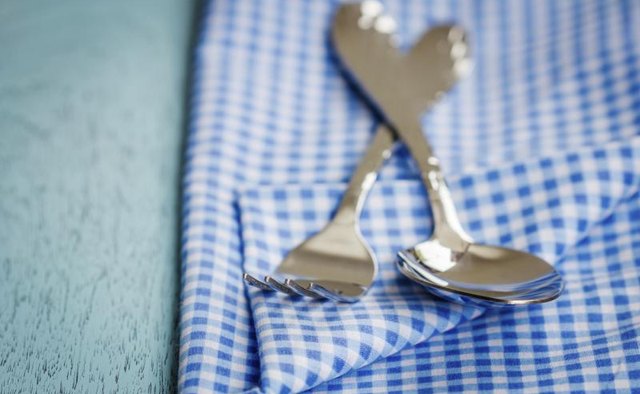 A spoon and fork on a blue tablecloth.