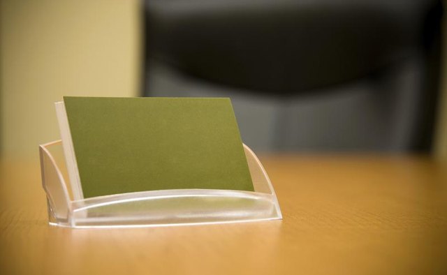A business card holder is holding blank cards on a desk.