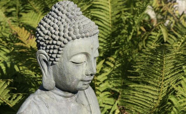 A Buddha statue in the garden with elongated ear lobes.