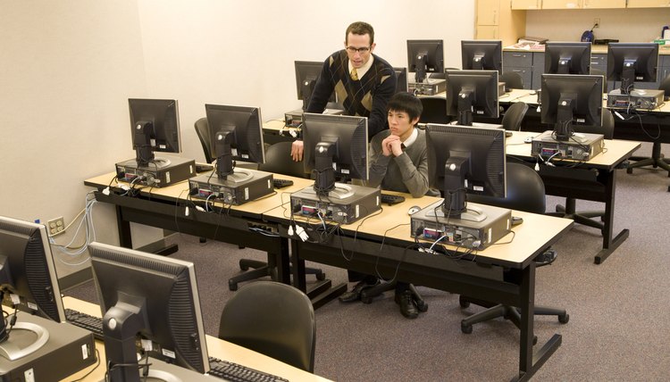 Teacher with school boy (16-17) working in computer room
