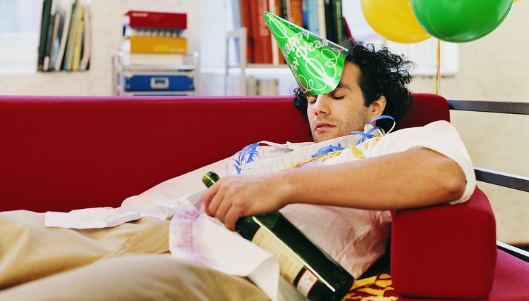 Businessman Asleep on an Office Sofa Holding a Bottle of Wine