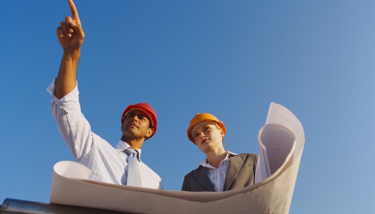 Low angle view of a young woman and a young man wearing hardhats holding design plans