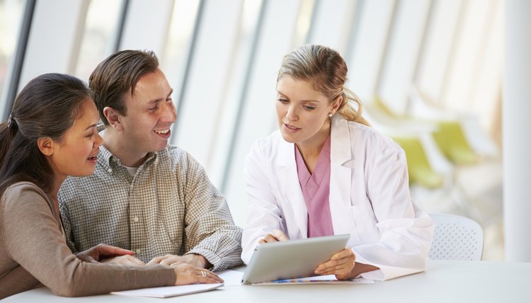 Female Doctor Using Digital Tablet Talking With Patients