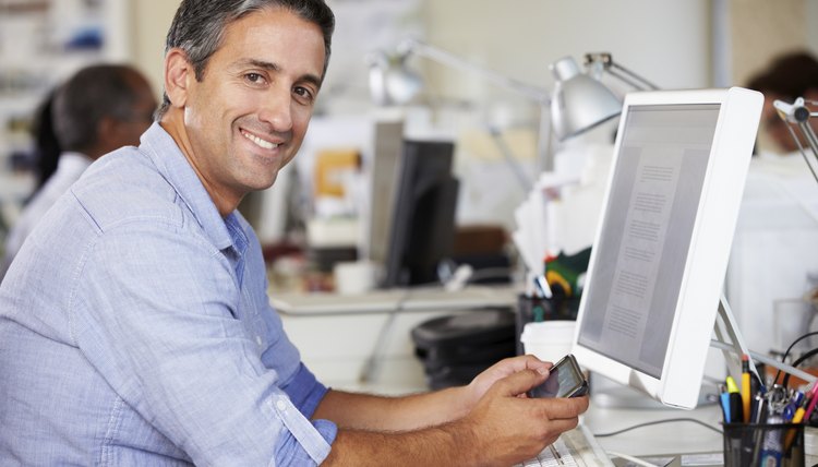 Man Using Mobile Phone At Desk In Busy Creative Office
