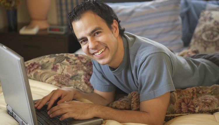 Portrait of a young man lying on the bed working on a laptop