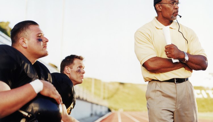 Football players with coach, watching game from side lines