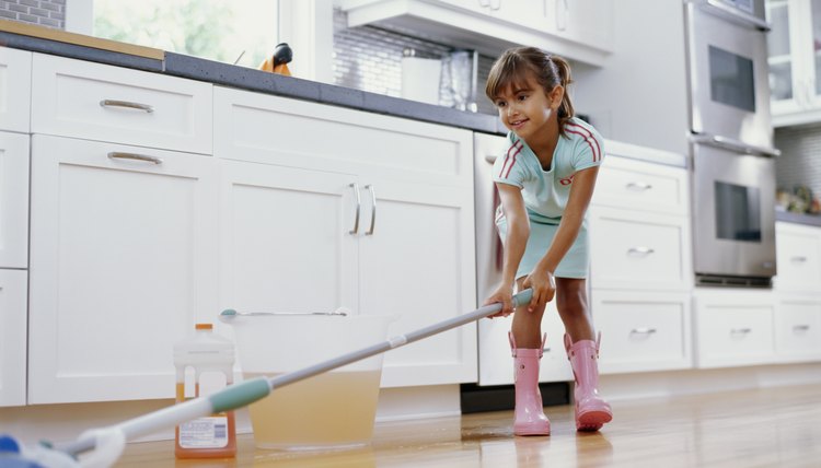 Girl (6-8) cleaning kitchen floor with mop, smiling, low angle view