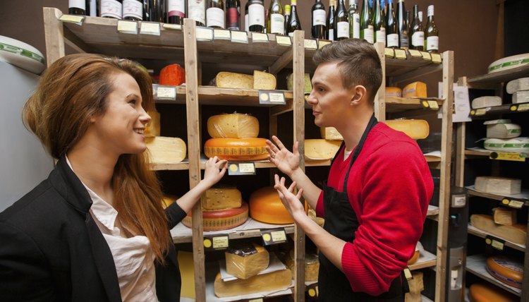 Male salesperson showing cheese to female customer in store