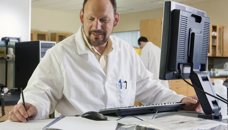 Lab technician working on a computer and writing experimental data in a notepad